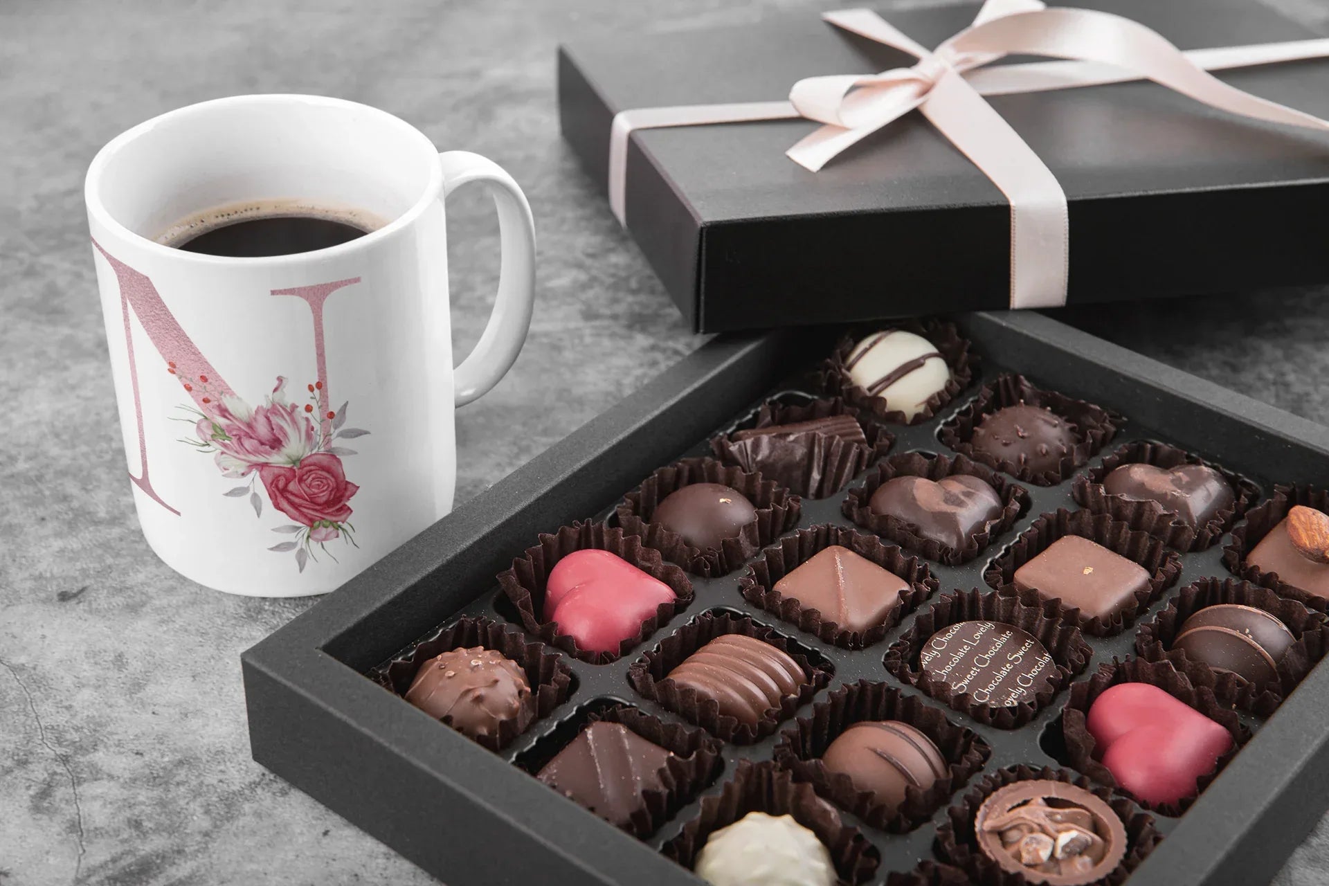 White mug with floral letter I design beside assorted chocolates in a gift box.