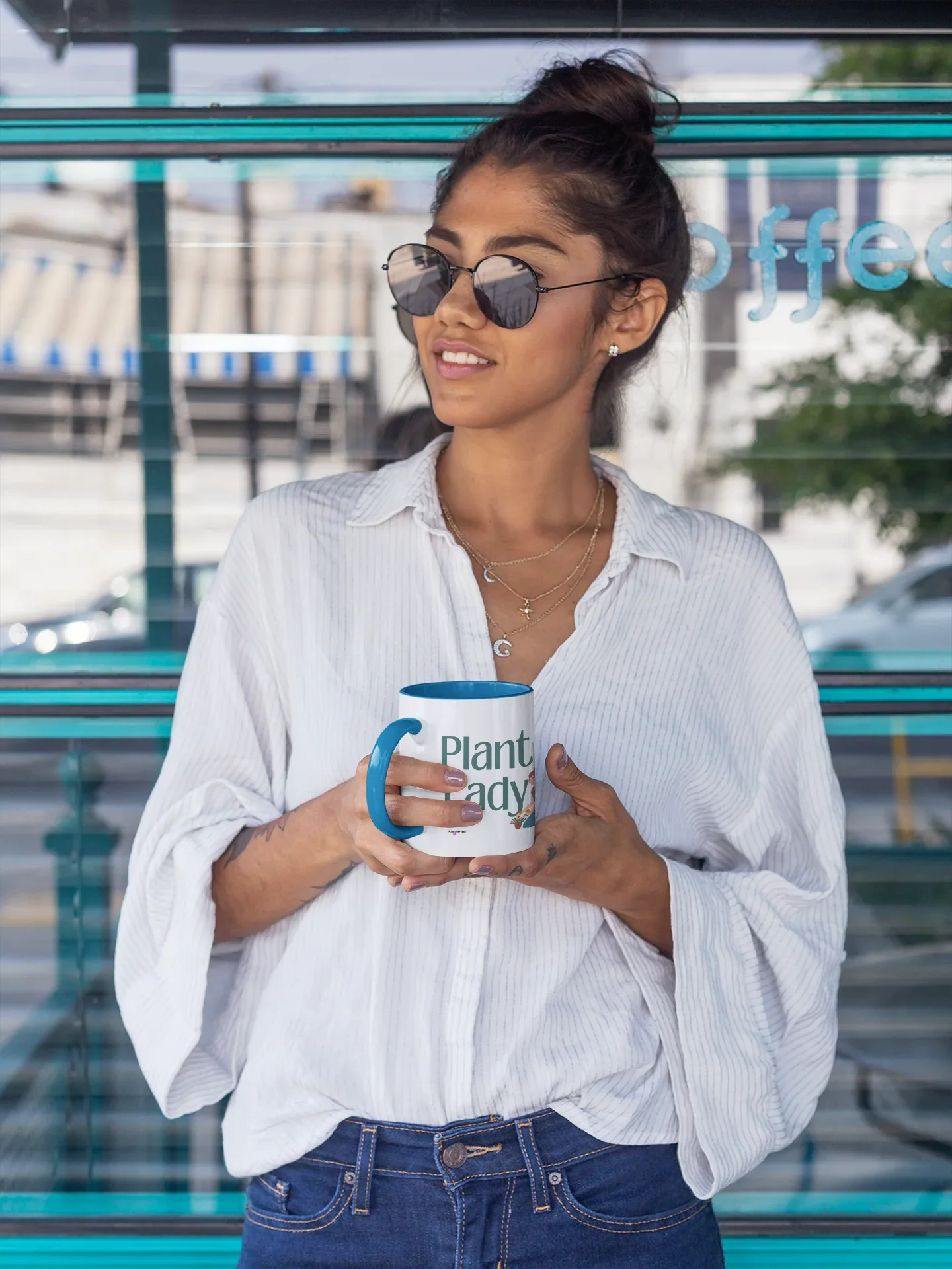 White ceramic coffee mug with blue handle, Plant Lady design held in cafe