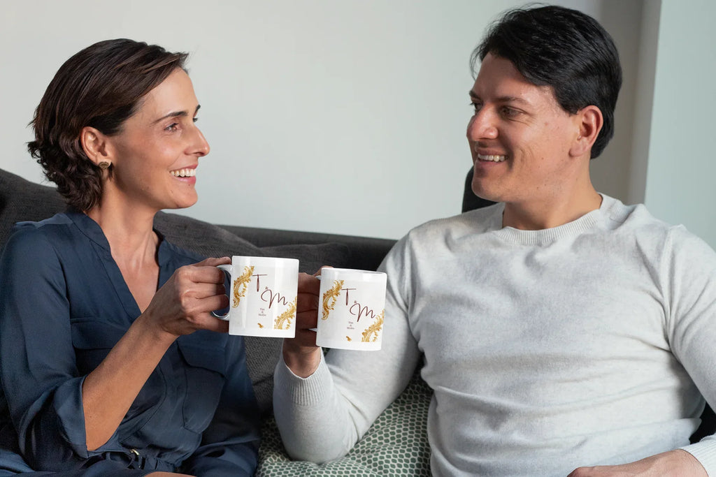 Two white wedding mugs with gold filigree and dark red 'T & M' printed