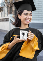 White ceramic graduation mug with printed cap, held in hands