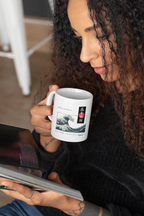 White mug with blue ocean wave print and red/black emblem, being sipped.