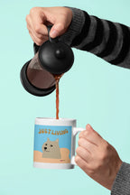 Ceramic mug with blue “JUST LIVING” dog design being filled from a kettle