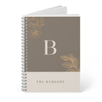 A5 notebook with taupe cover, gold monogram B, floral motifs, and stacked spiral binding.
