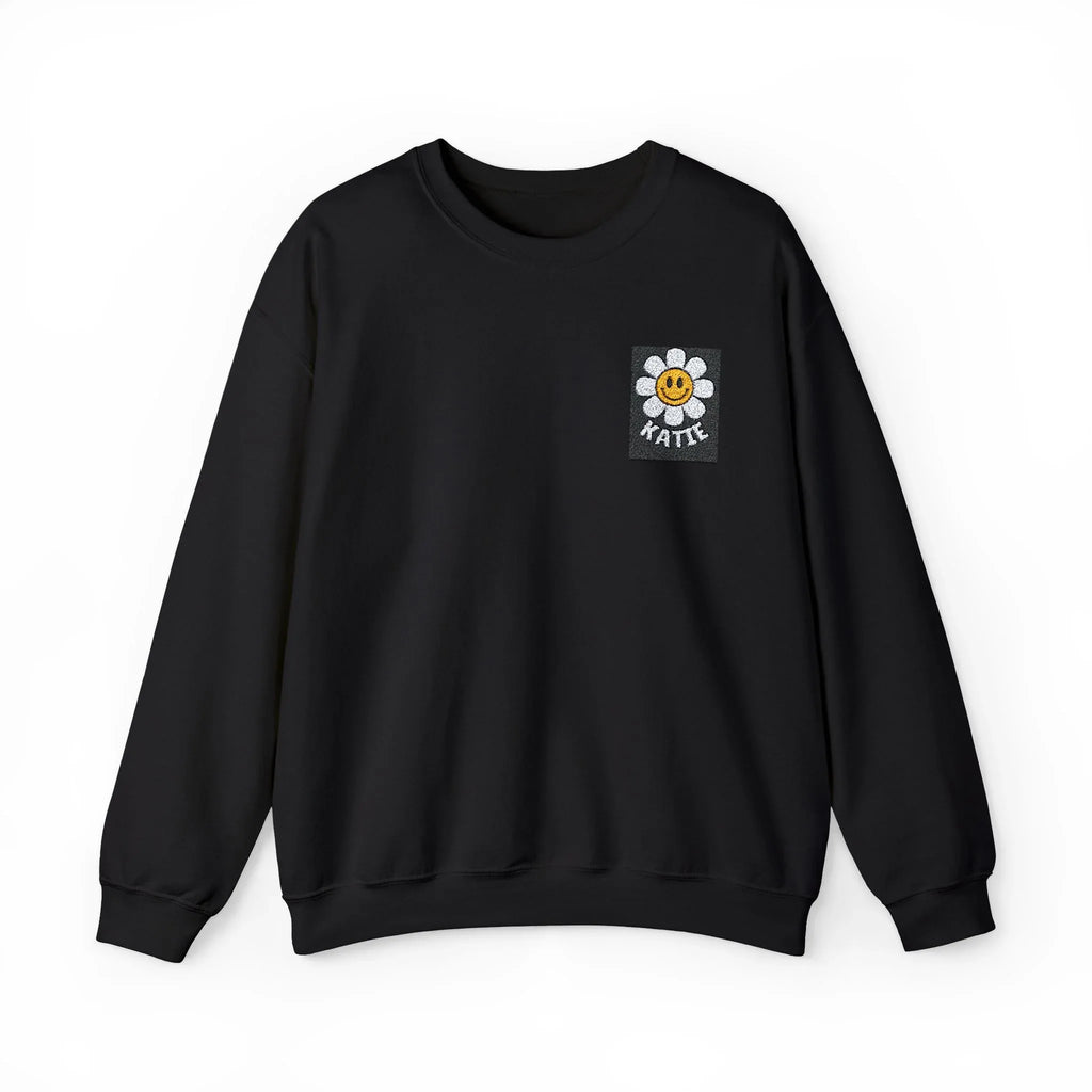 Black crewneck sweatshirt with small square flower smiley patch on chest.