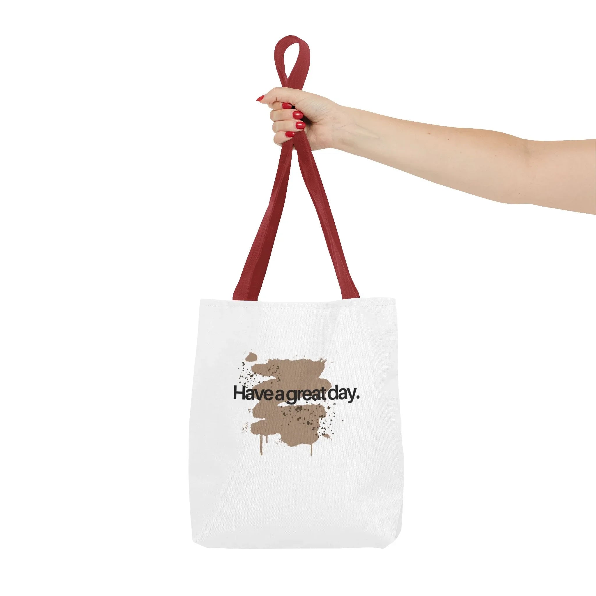 Red canvas tote bag held by top handles, showing brown splash “Haveagreatday.”
