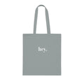 Light gray cotton tote bag with custom text "hey."