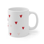 White mug with scattered red and light-pink hearts pattern and curved white handle.
