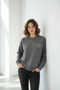 Dark gray crewneck sweatshirt with small chest text, worn by a model
