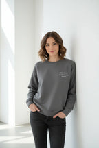 Dark gray crewneck sweatshirt with small chest text, worn by a model
