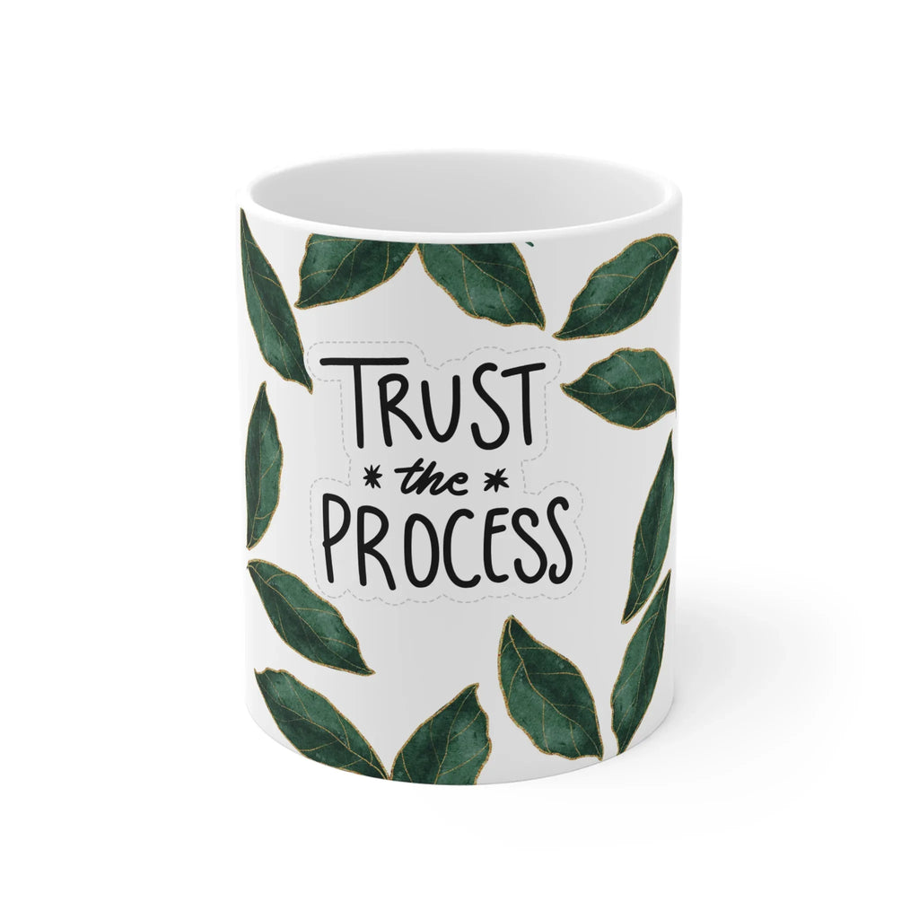 White mug with green leaves framing “TRUST” and “the PROCESS” on the front