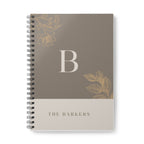 A5 notebook with taupe cover, gold monogram B, and floral corner accents; spiral binding.