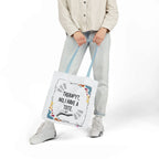 White canvas tote bag with printed quote and colorful doodles, hanging from hands.