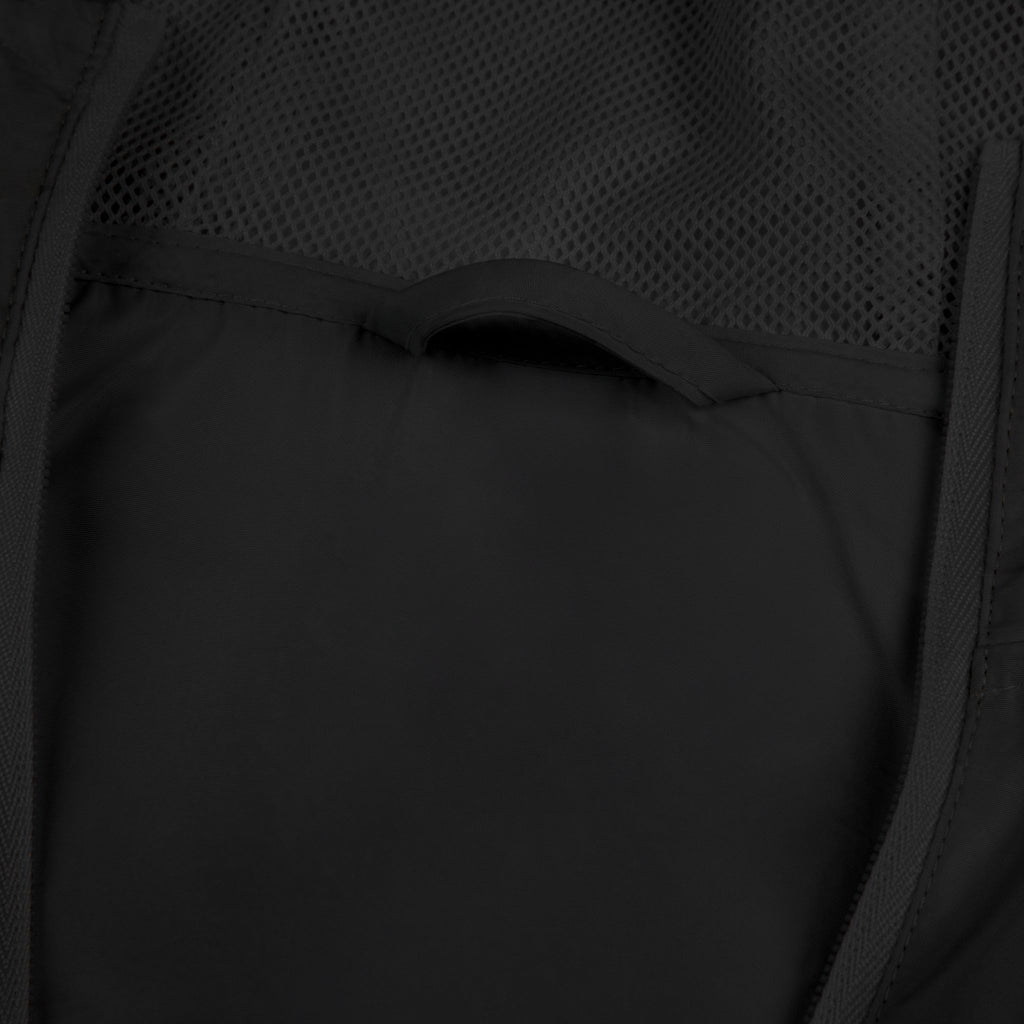 Black windbreaker jacket close-up: vented mesh panel and curved pocket seam detail.