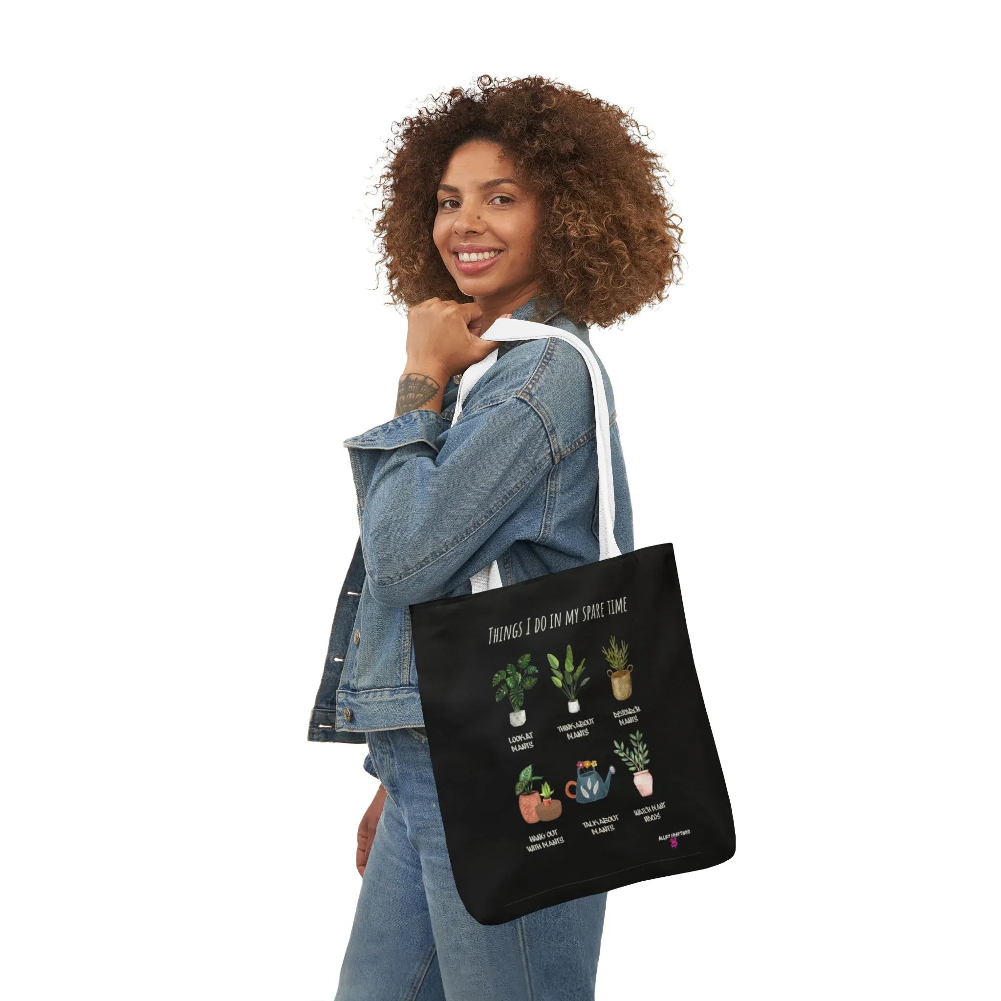 Black tote bag with white handles and plant collage print, carried on shoulder.