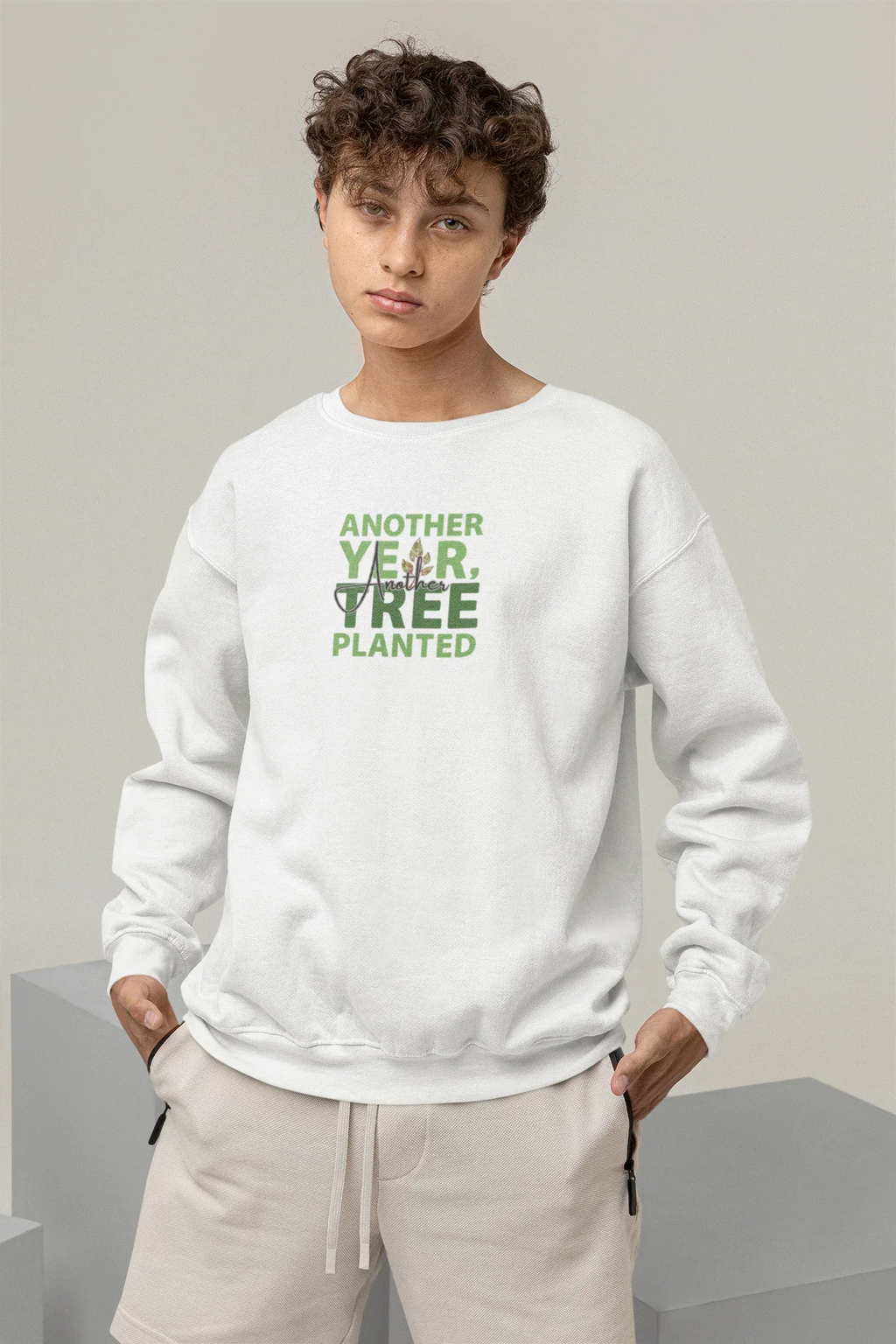 White crewneck sweatshirt worn by model with green “Another Year, Tree Planted” chest graphic.