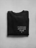 Black crewneck sweatshirt with front text graphic reading “I SURVIVED ANOTHER YEAR”