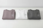 Folded crewneck sweatshirts in mauve, white, and dark gray with small chest text