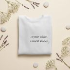 White crewneck sweatshirt with a year wiser, a world kinder print