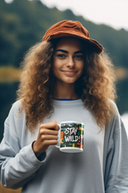 White ceramic mug with 'STAY WILD!' graphic, held up by person