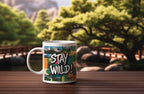 White ceramic mug with 'Stay Wild!' landscape print, side view with curved handle