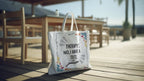 White canvas tote bag with printed text and colorful doodles, long top handles.