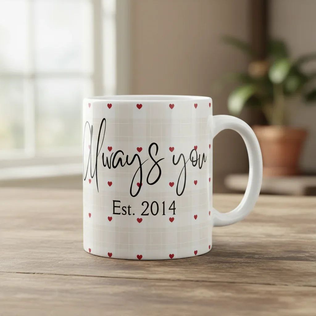 White mug with red hearts, black cursive print and “Est. 2014” on front, on tabletop.
