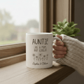 White ceramic mug with auntie quote held by person in a sweater sleeve