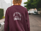 Burgundy sweatshirt with “Easily Distracted by Snails” graphic on the back.