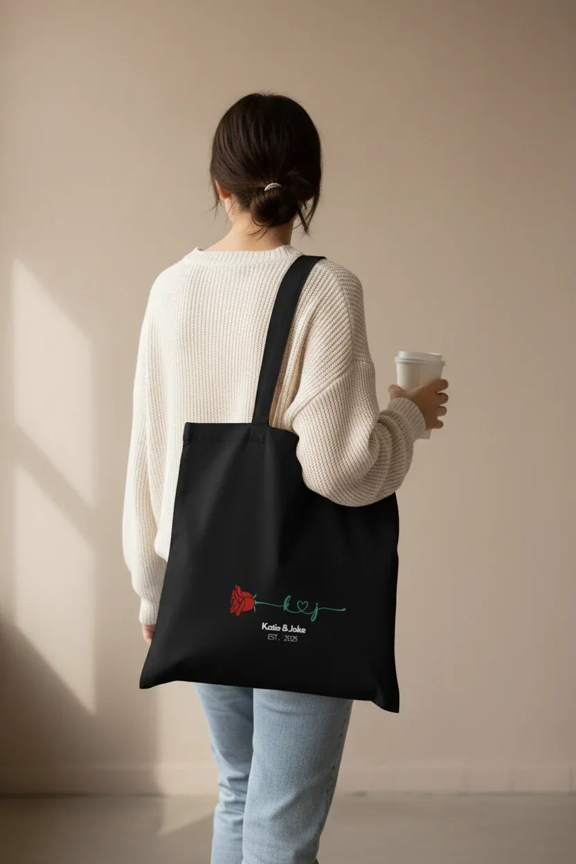Black personalized tote bag back view with red rose print and 'Katie&Jake' text
