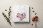 White crewneck sweatshirt with “Birthday Girl” text and colorful floral heart graphic