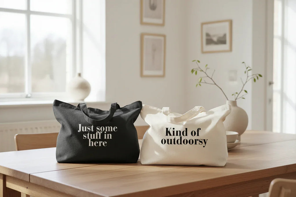 Two cotton tote bags in black and cream, with text “Just some stuff in here” and “Kind of outdoorsy”.