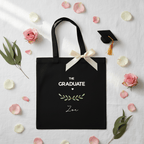 Black canvas tote bag with graduation emblem, ribbon bow, and name 'Loe'