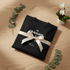 Black canvas tote bag with printed graduation logo and ribbon bow, flat lay