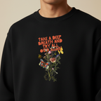 Black crewneck sweatshirt close-up with colorful “Take a Deep Breath” floral graphic.