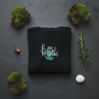 Black mindfulness hoodie with “Just breathe” slogan and hand heart graphic on chest