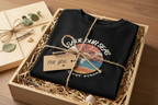 Black graphic T-shirt with circular ocean sunset logo and a small gift tag attached