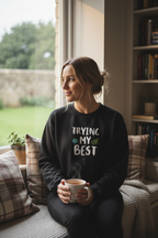 Black sweatshirt on woman sitting, 'TRYING MY BEST' quote with globe-and-leaves