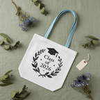 White graduation tote bag with light blue handles and 'Class of 2026' wreath print