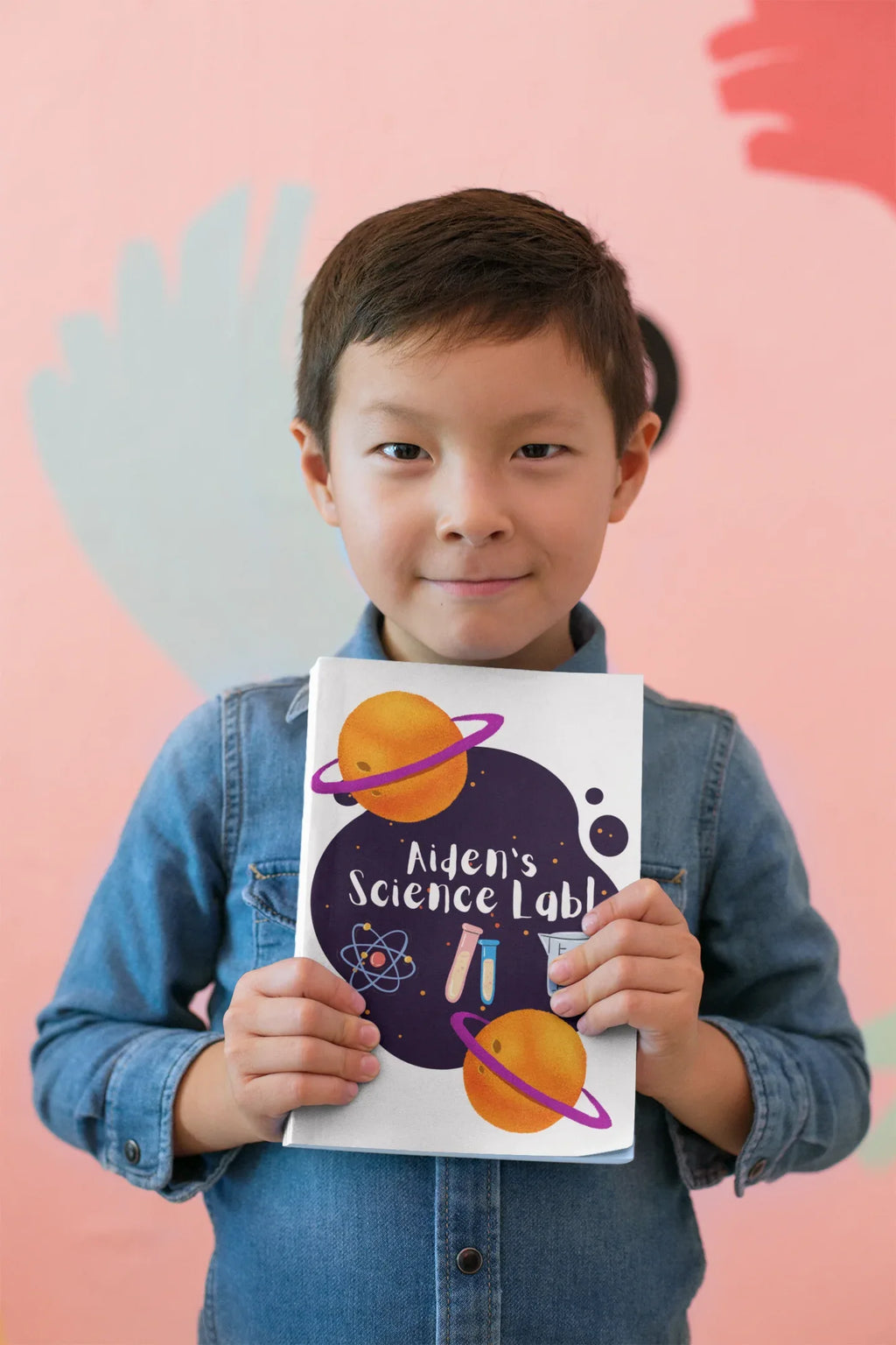 Child holding a science-themed journal with purple heart design and “Alien’s Science Lab!”