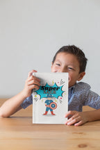 Superhero journal with colorful comic cover, child holding it on a desk