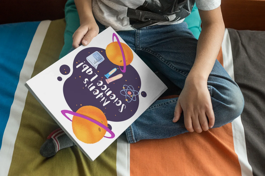 Hands holding a science-themed journal with purple heart, planets, and “Harvey’s Science Lab!”