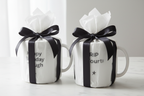 Two coffee mugs wrapped in white gift wrap with black ribbon; one reads Happy Birthday Though