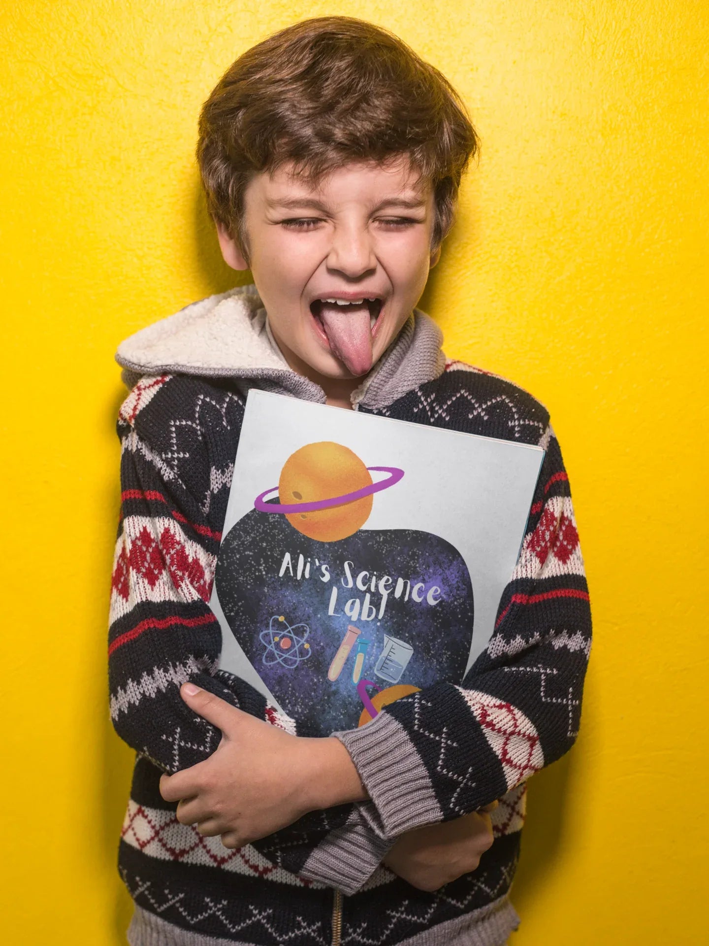 Child holding a science-themed journal with purple heart, planets, and “Alien’s Science Lab!”