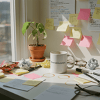 White ceramic mug on busy desk, handle visible, printed “Overstimulated.”