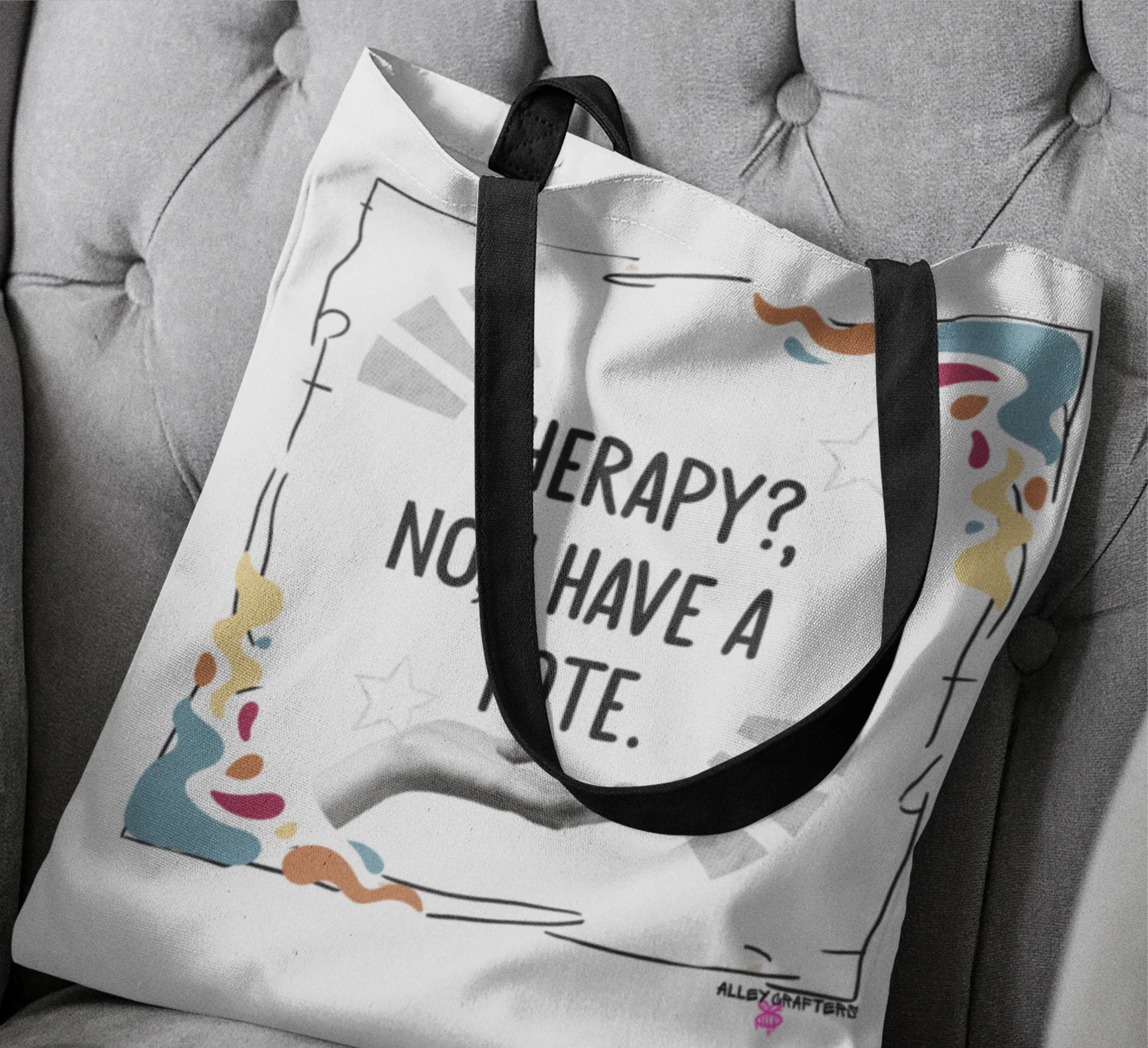 White tote bag on sofa cushion with black handles and printed quote plus doodles.