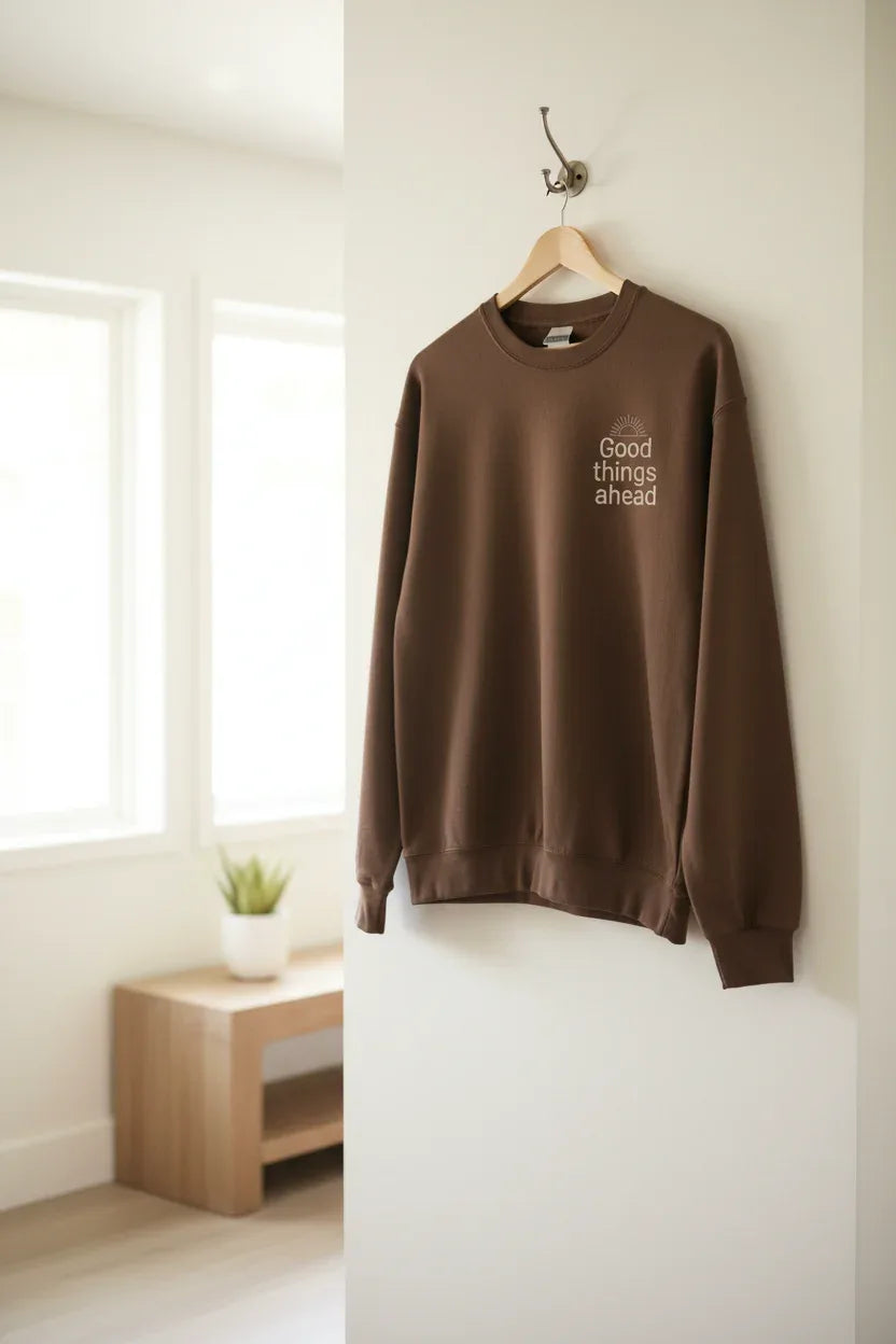Brown crewneck sweatshirt hanging on a wooden hanger with small chest logo