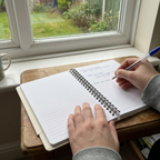 Lined nature notebook with spiral binding, open pages, and pen writing on a desk.