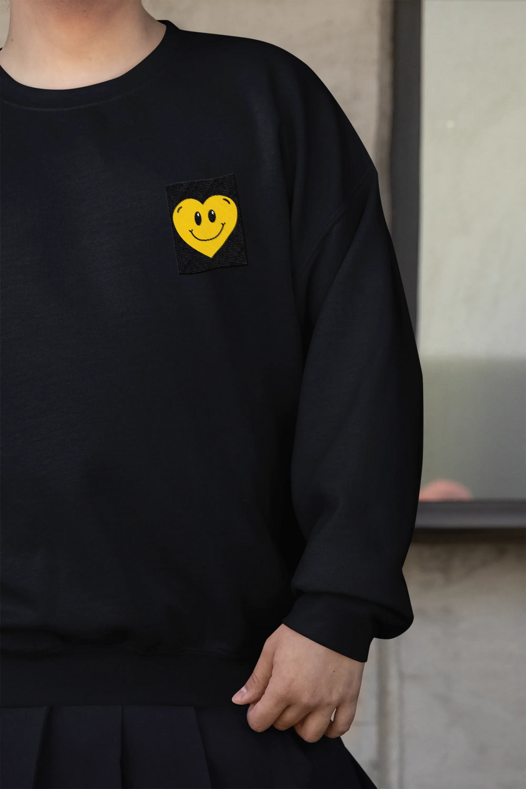 Black crewneck sweatshirt with embroidered smiley heart patch on left chest