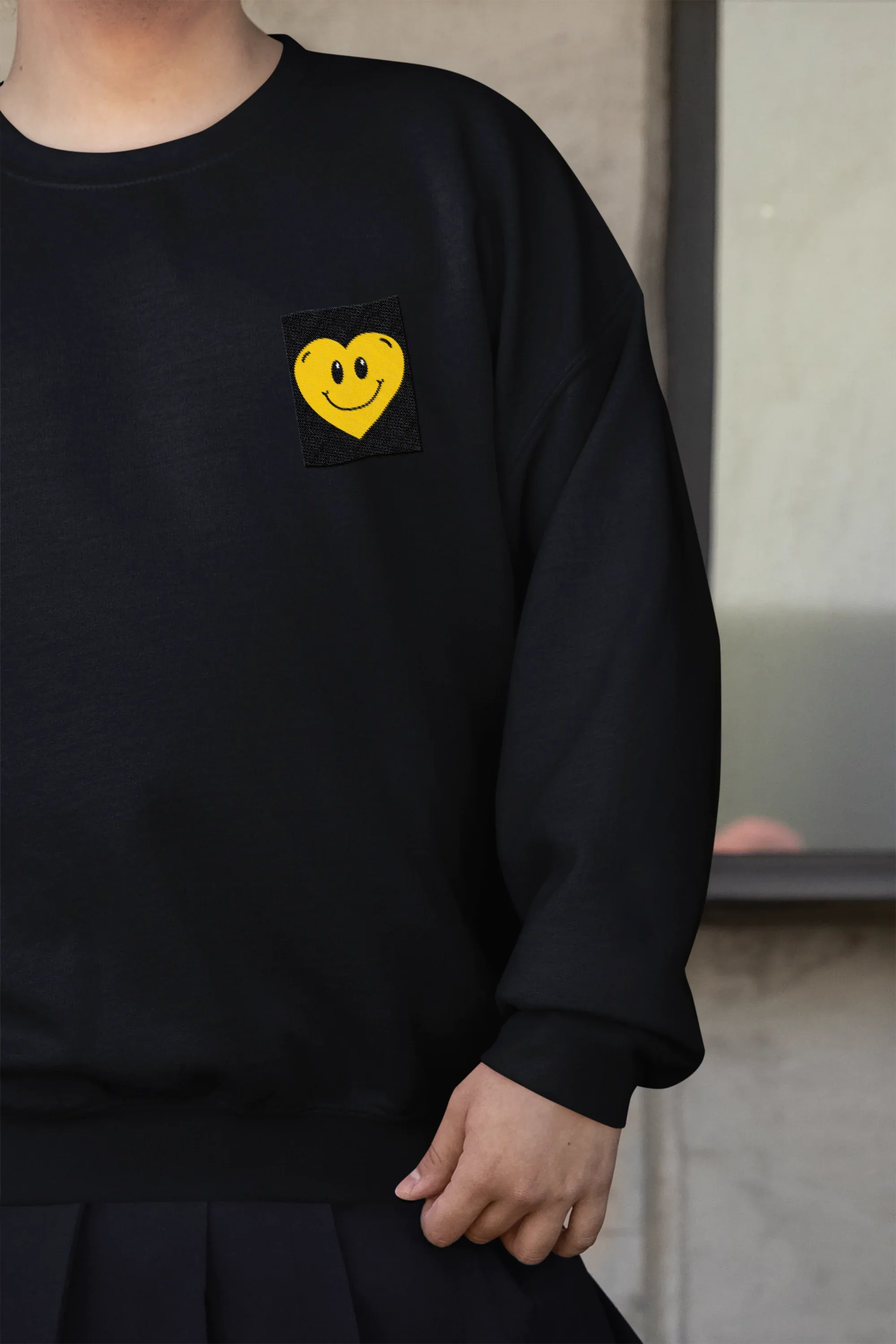 Black crewneck sweatshirt with embroidered smiley heart patch on left chest