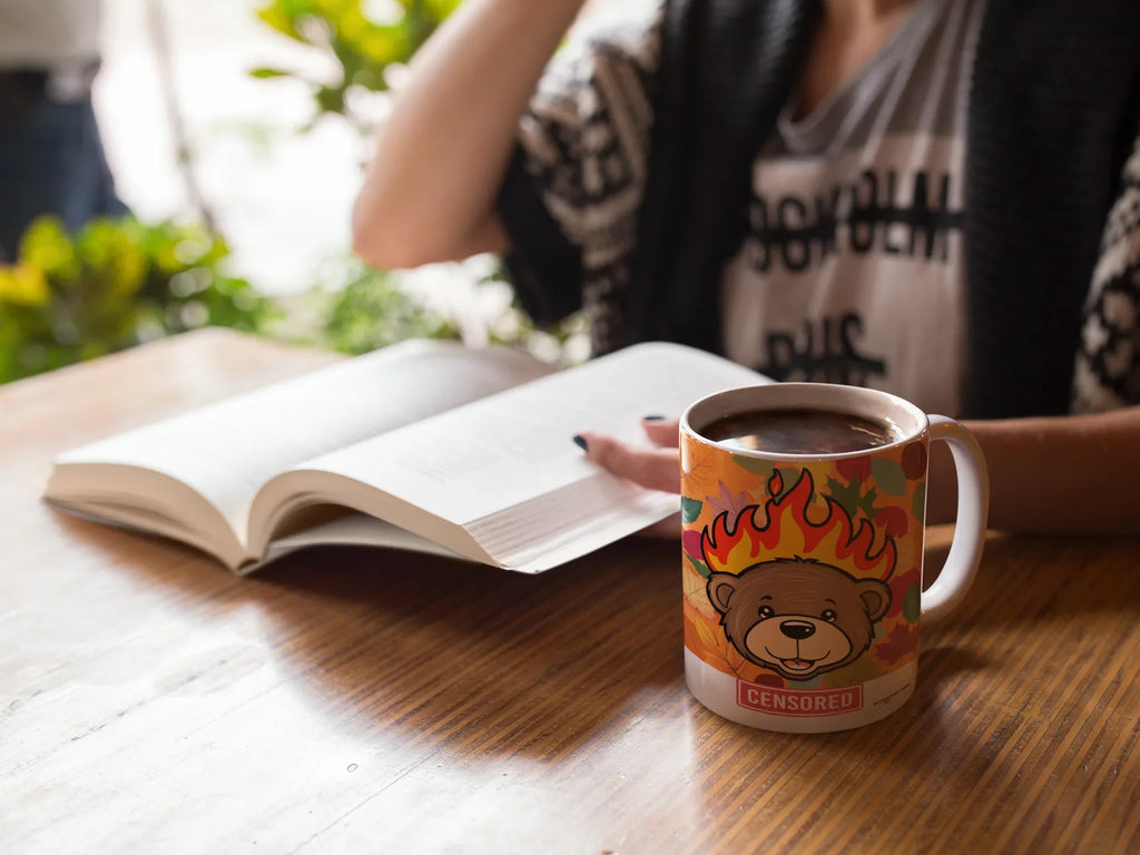 Hand holding a white bear mug with flames graphic and red “CENSORED” label.